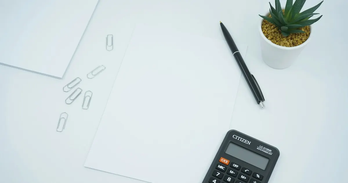 Calculadora e caneta sobre uma folha em branco em mesa de trabalho.