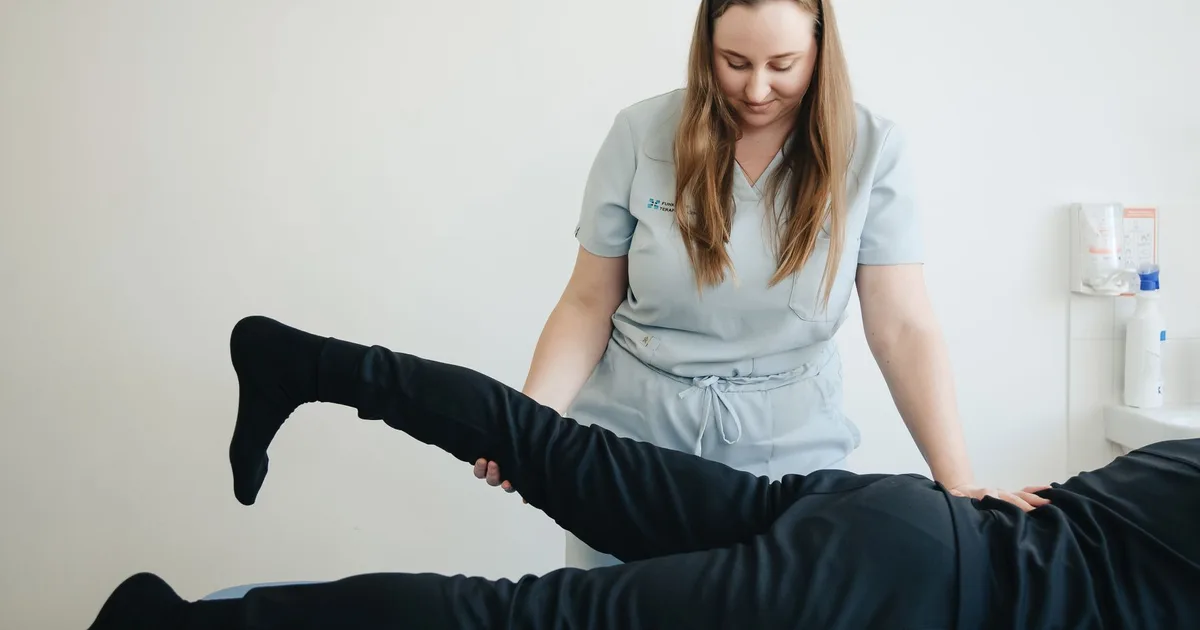 Fisioterapeuta elevando a perna de um paciente deitado durante a sessão