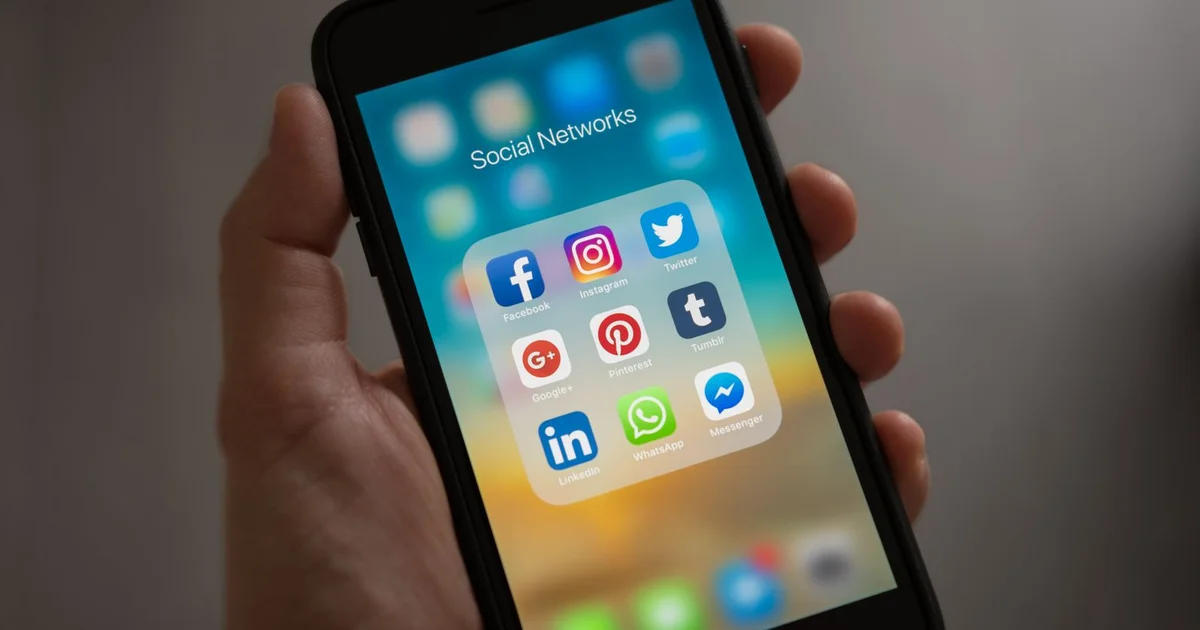Mão segurando celular com pasta de redes sociais aberta, incluindo WhatsApp